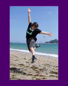 A boy with Downs Syndrome is leaping in the air on a beach